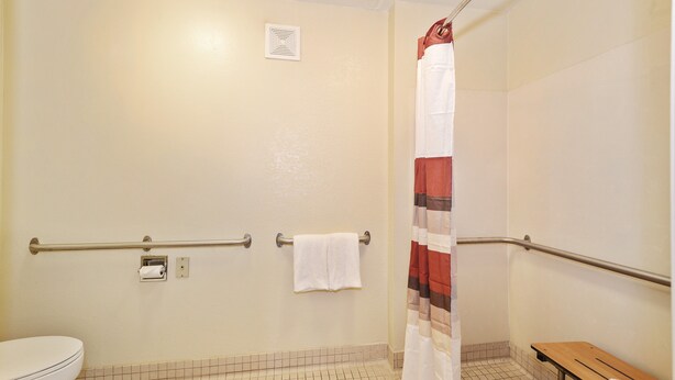 Un baño con inodoro, ducha con cortina a rayas y un banco.