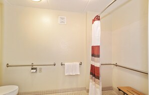 A bathroom with a toilet, a shower with a striped curtain, and a bench. - Red Roof Inn Albany Airport (Albany)