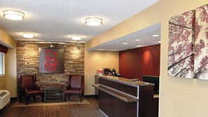 Zona de recepción con pared de piedra, un cartel rojo, dos sillones de cuero, mostrador de recepción y una máquina de café.