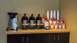 Una estación de café con cafetera, varios dispensadores de café, vasos desechables y diferentes opciones de leche para café.