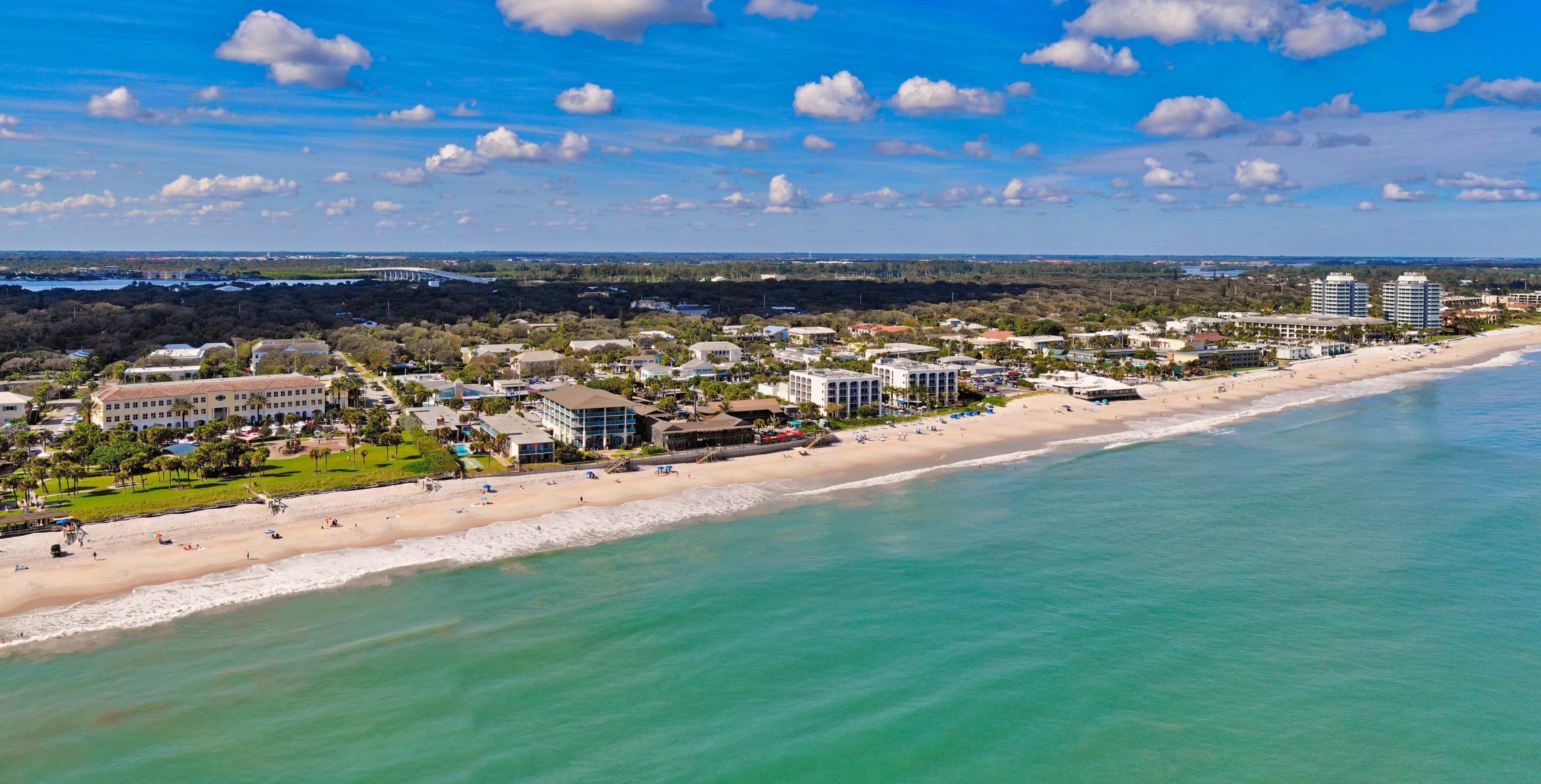 A coastal cityscape with a beach, buildings, and a bridge in the distance.