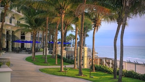 A resort with palm trees, outdoor seating, and a view of the ocean.
