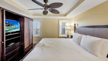 A hotel room with a bed, a television, a ceiling fan, and a window with blinds.