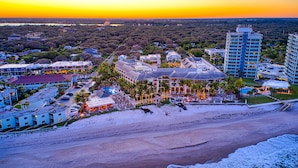 An aerial view of a coastal resort with multiple buildings, a beachfront, and a clear view of the ocean.
