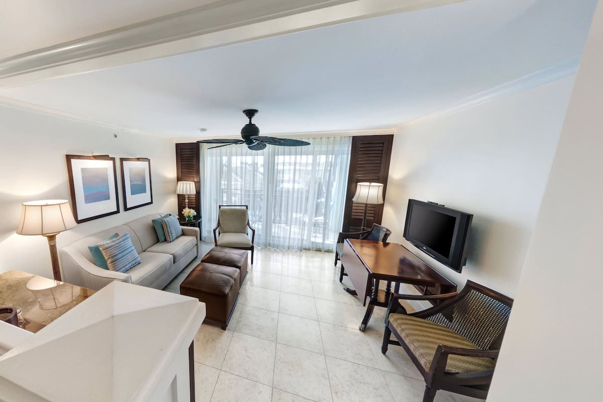 A modern living room with a sofa, armchairs, a coffee table, a TV, and a ceiling fan.