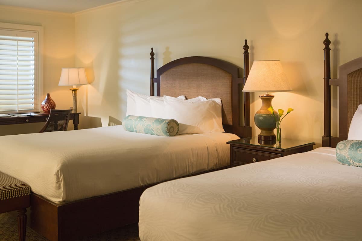 A hotel room with two beds, a nightstand, a lamp, and a vase with flowers.