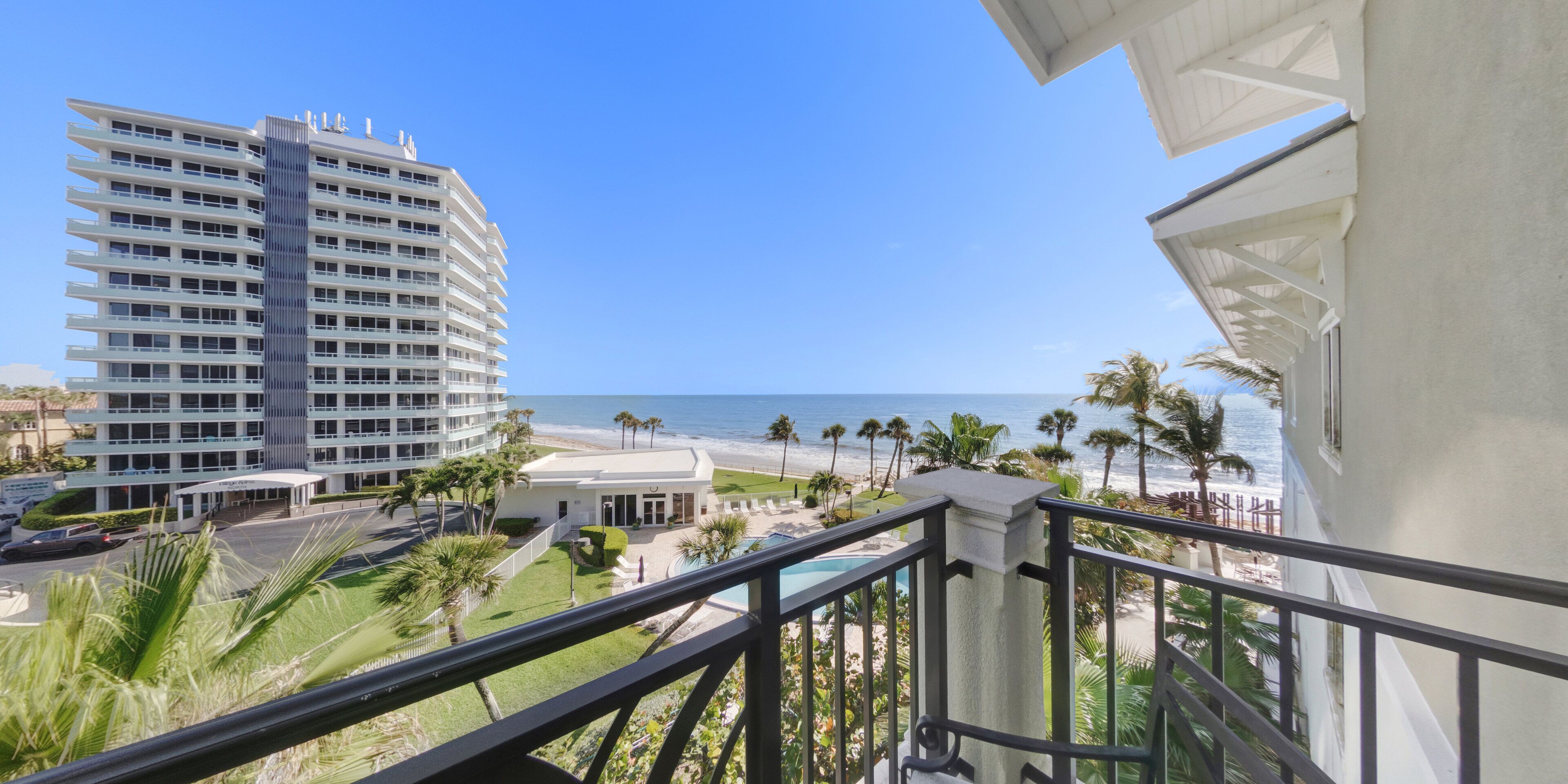 A high-rise hotel with a pool, beach view, and palm trees.