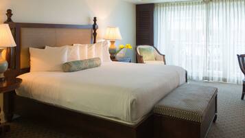 A large bed with multiple pillows, a nightstand with a lamp, a chair, and a window with curtains.