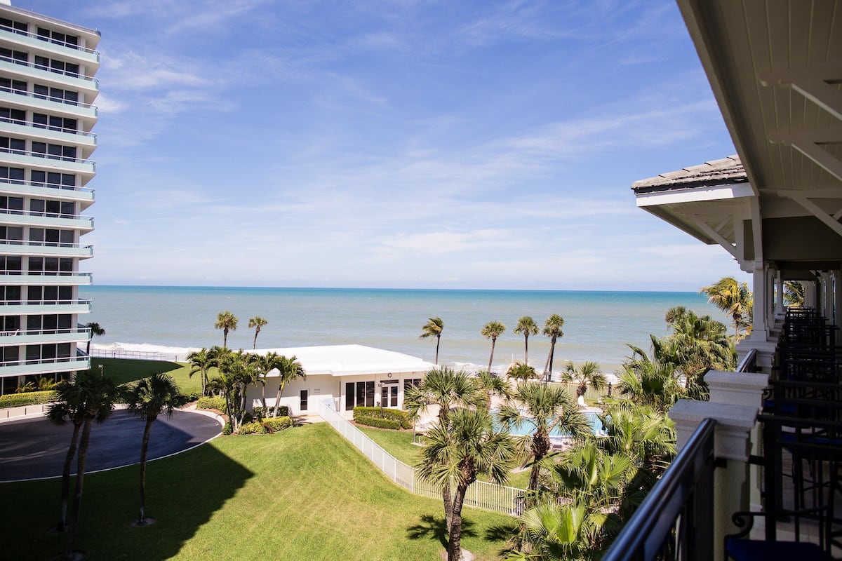 A hotel with a view of the ocean, palm trees, and a pool area.