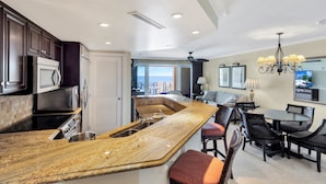A modern kitchen with a large island, dark wood cabinets, stainless steel appliances, and a view to the outside.