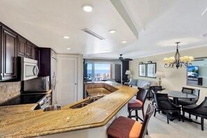 Une cuisine moderne dotée d’un grand îlot central, de meubles en bois foncé, d’appareils électroménagers en acier inoxydable et offrant une vue sur l’extérieur.