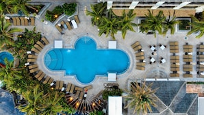 Vue aérienne d’un complexe hôtelier doté d’une piscine centrale, de plusieurs espaces de détente avec des chaises longues et entouré de palmiers.