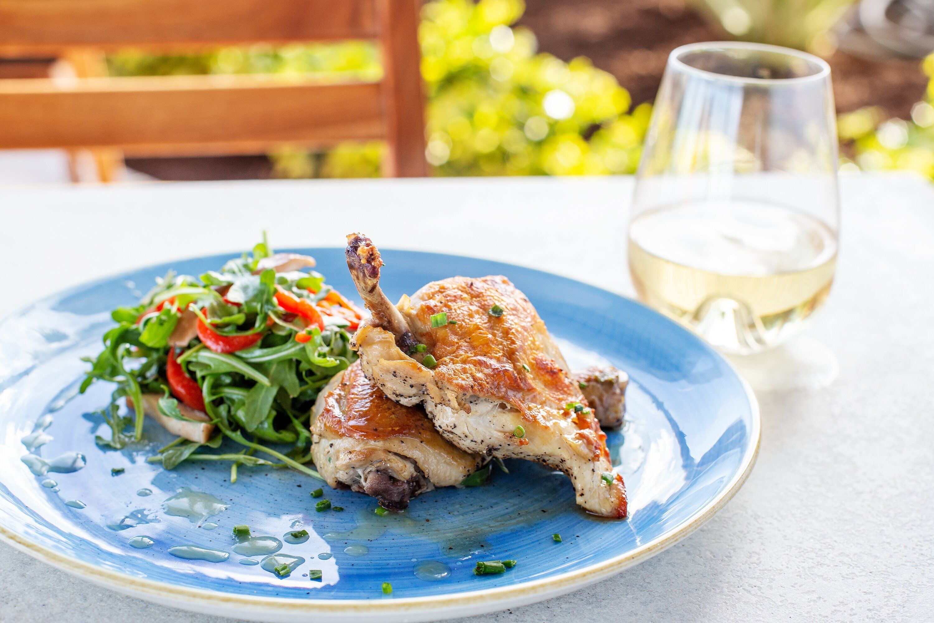 A plate with roasted chicken and salad, and a glass of white wine on a table.