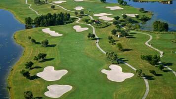 An aerial view of a golf course with sand bunkers, water bodies, and scattered trees.