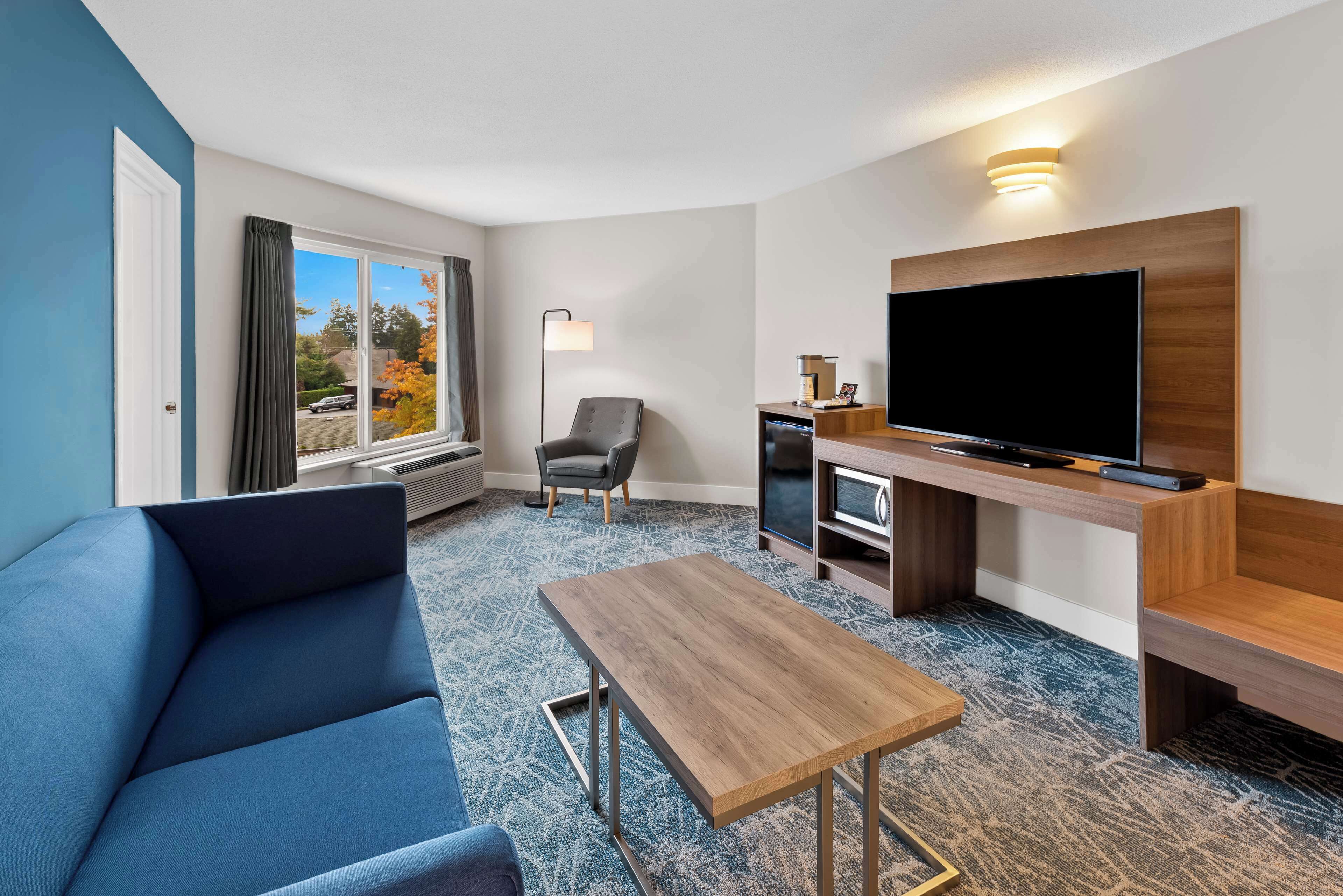Une chambre d’hôtel avec un canapé bleu, une table basse en bois, une télévision et un bureau avec une lampe.