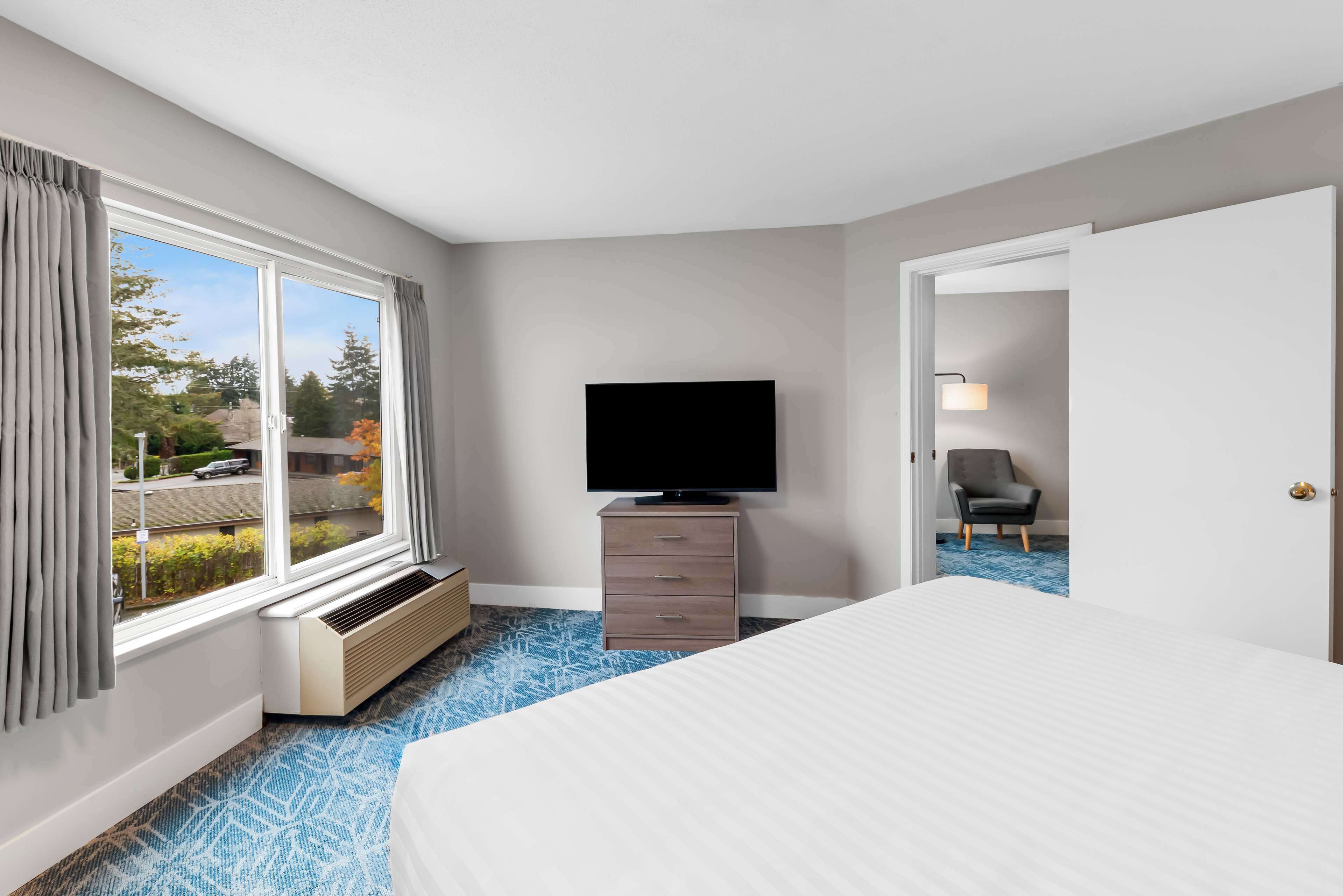 Een hotelkamer met een groot bed, een flatscreen televisie op een dressoir, een raam met gordijnen en uitzicht op de omgeving.