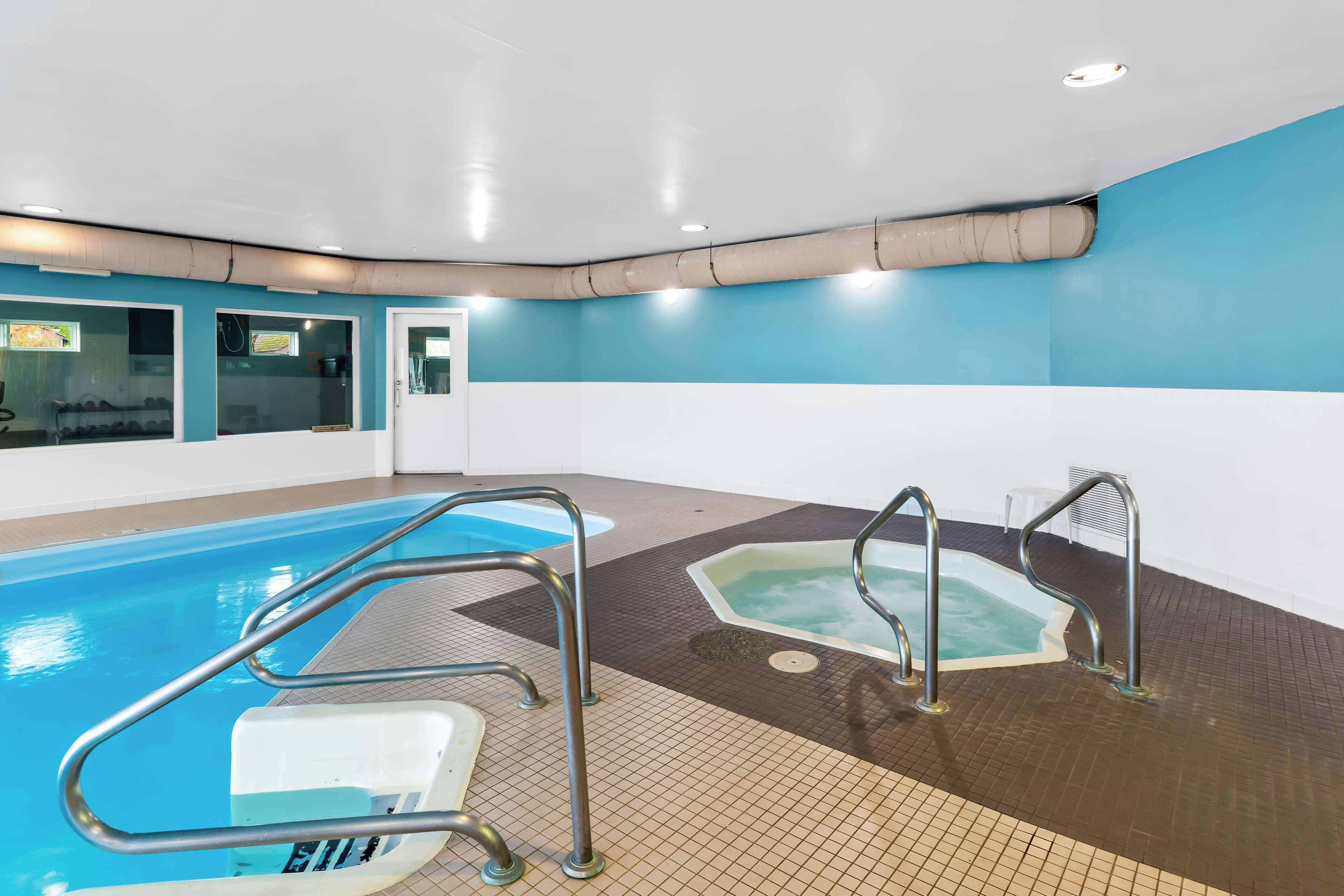 An indoor swimming pool with clear water, a diving board, and two hot tubs.