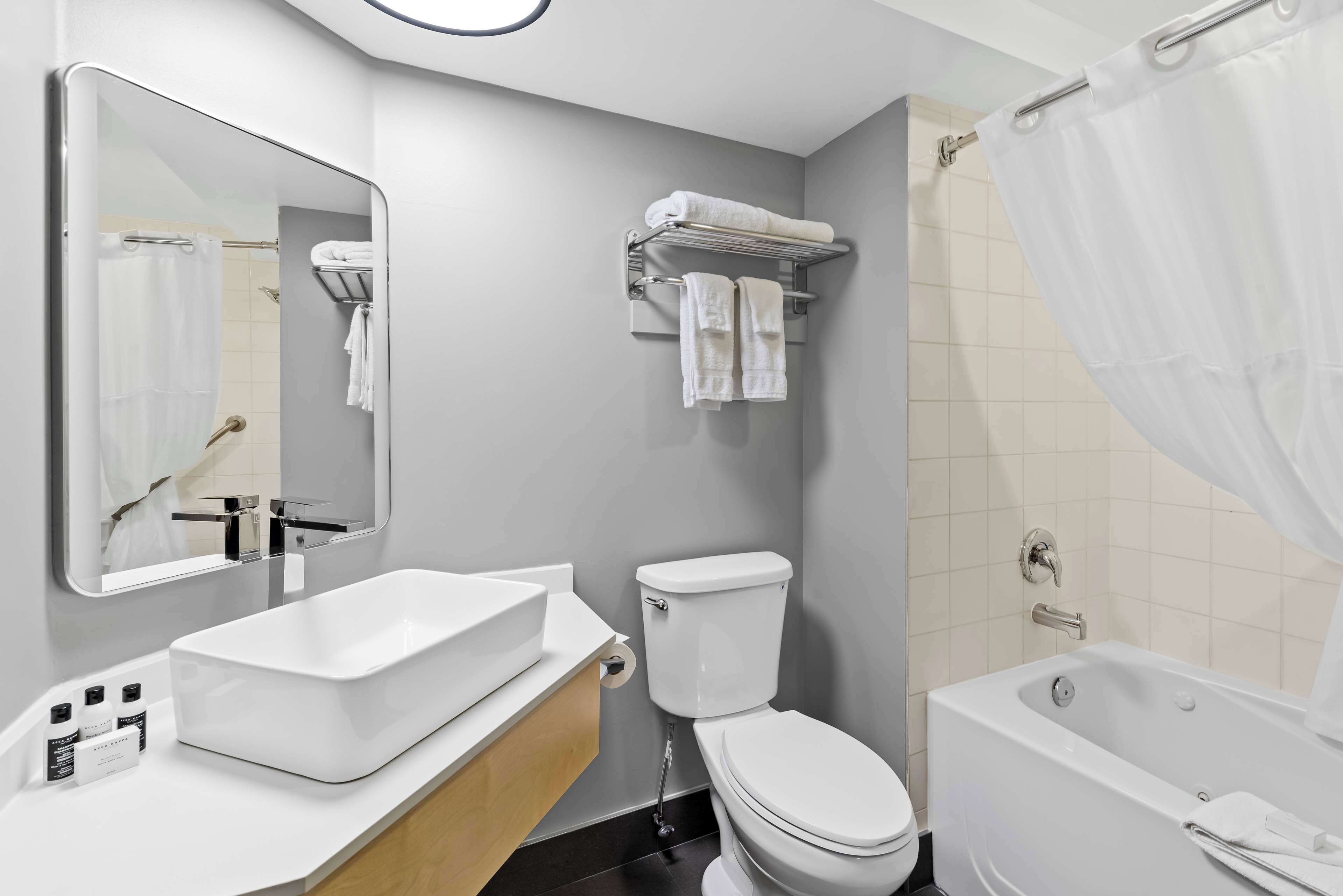 A modern bathroom with a white sink, toilet, and bathtub. There are towels on a rack and a shower curtain.