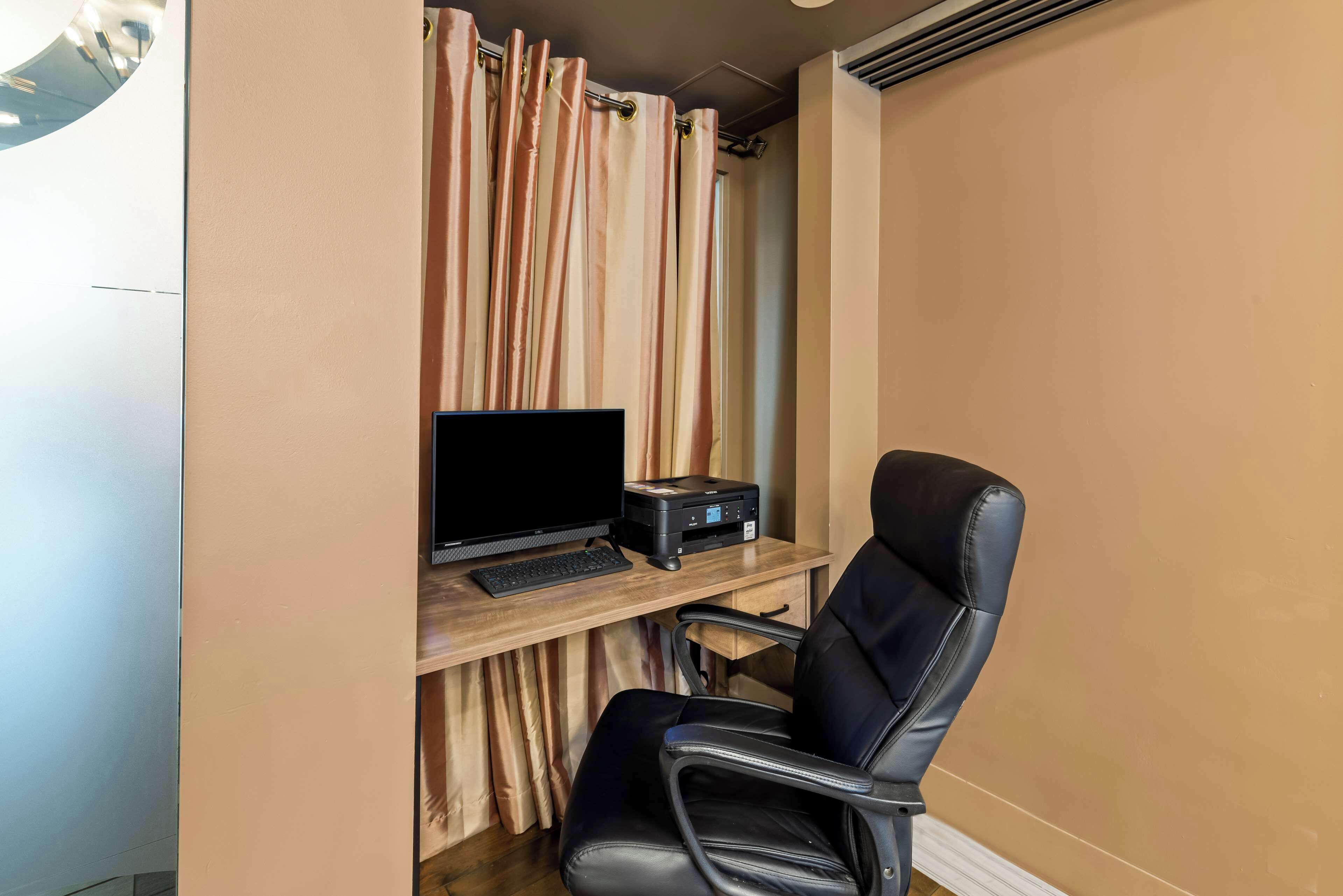 Una habitación con un escritorio, una computadora, una impresora y una silla de cuero negro.