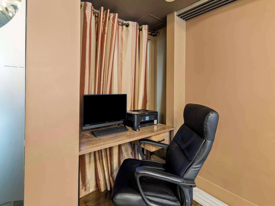 A room with a desk, a computer, a printer, and a black leather chair.
