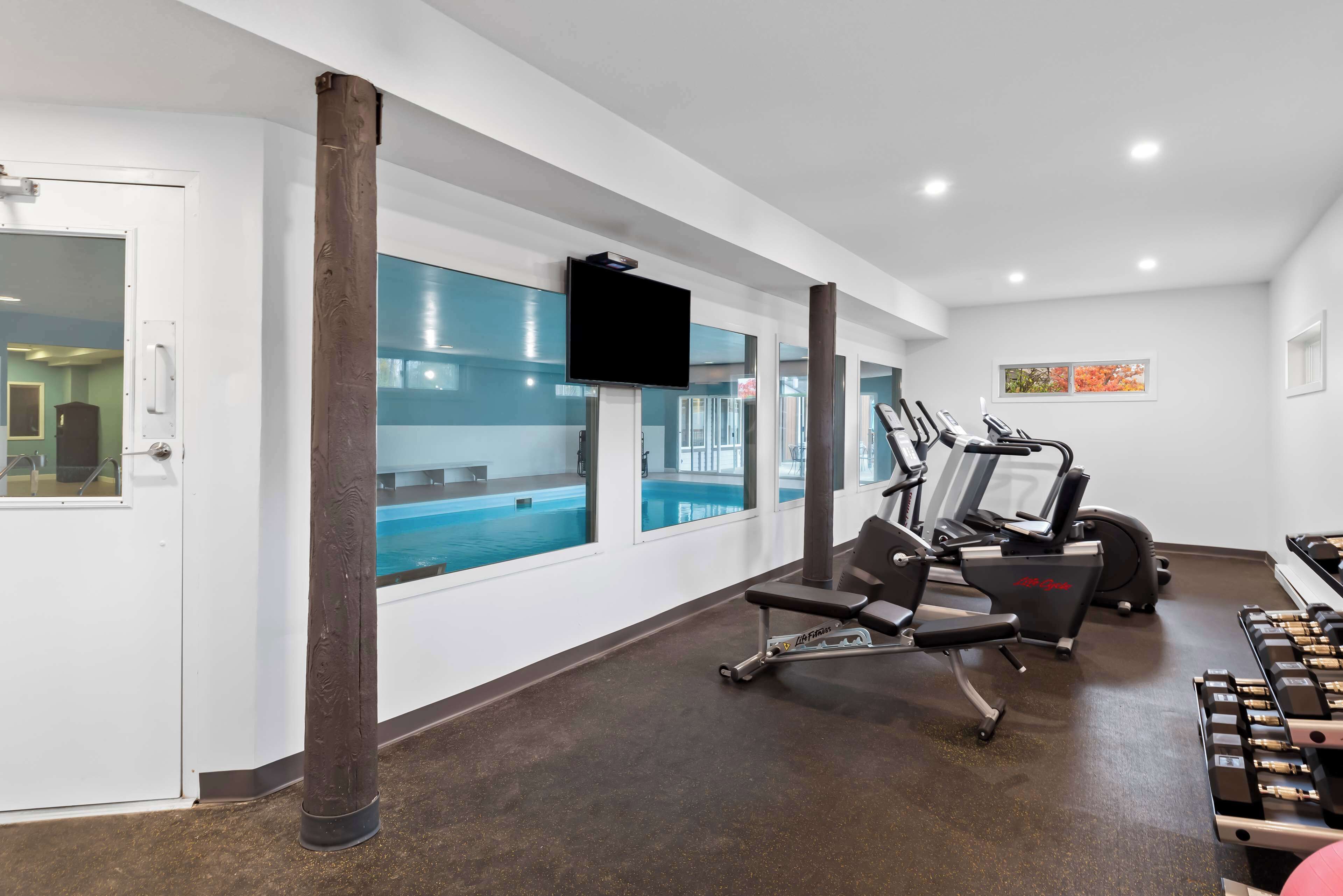 A gym with exercise equipment, a television, and a view of an indoor pool.