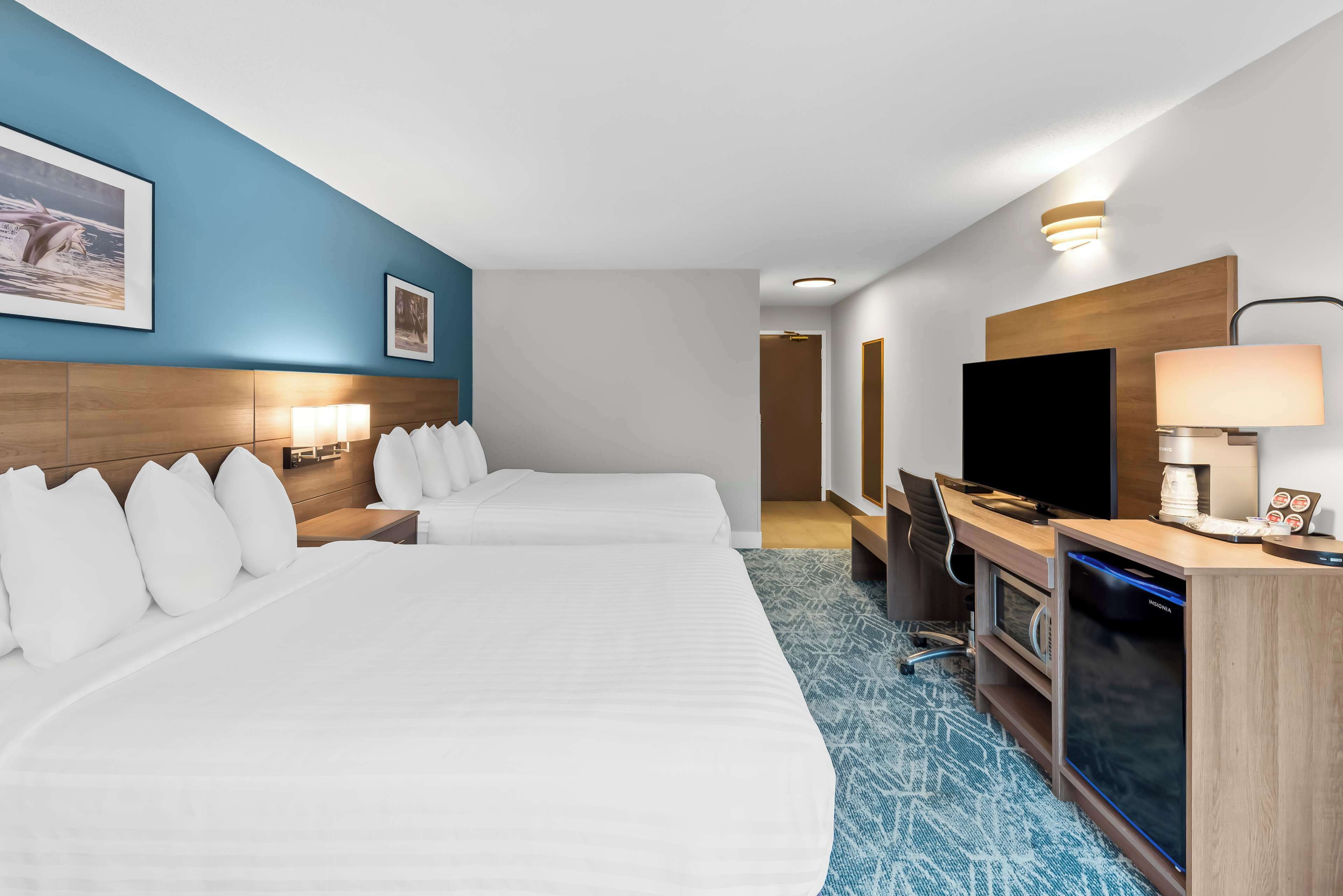 Habitación de hotel con dos camas, un escritorio con computadora, un televisor y la puerta del baño.