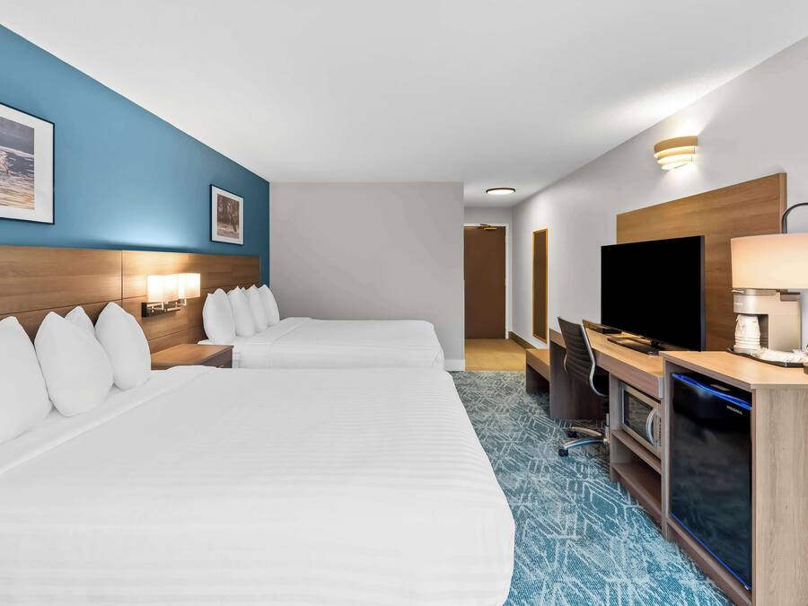 Habitación de hotel con dos camas, un escritorio con computadora, un televisor y la puerta del baño.