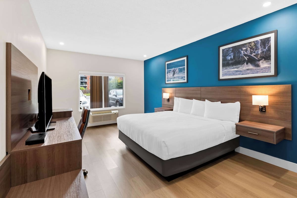Ein modernes Hotelzimmer mit einem großen Bett, einem Flachbildfernseher, einem Schreibtisch und einem Fenster mit Blick nach außen.