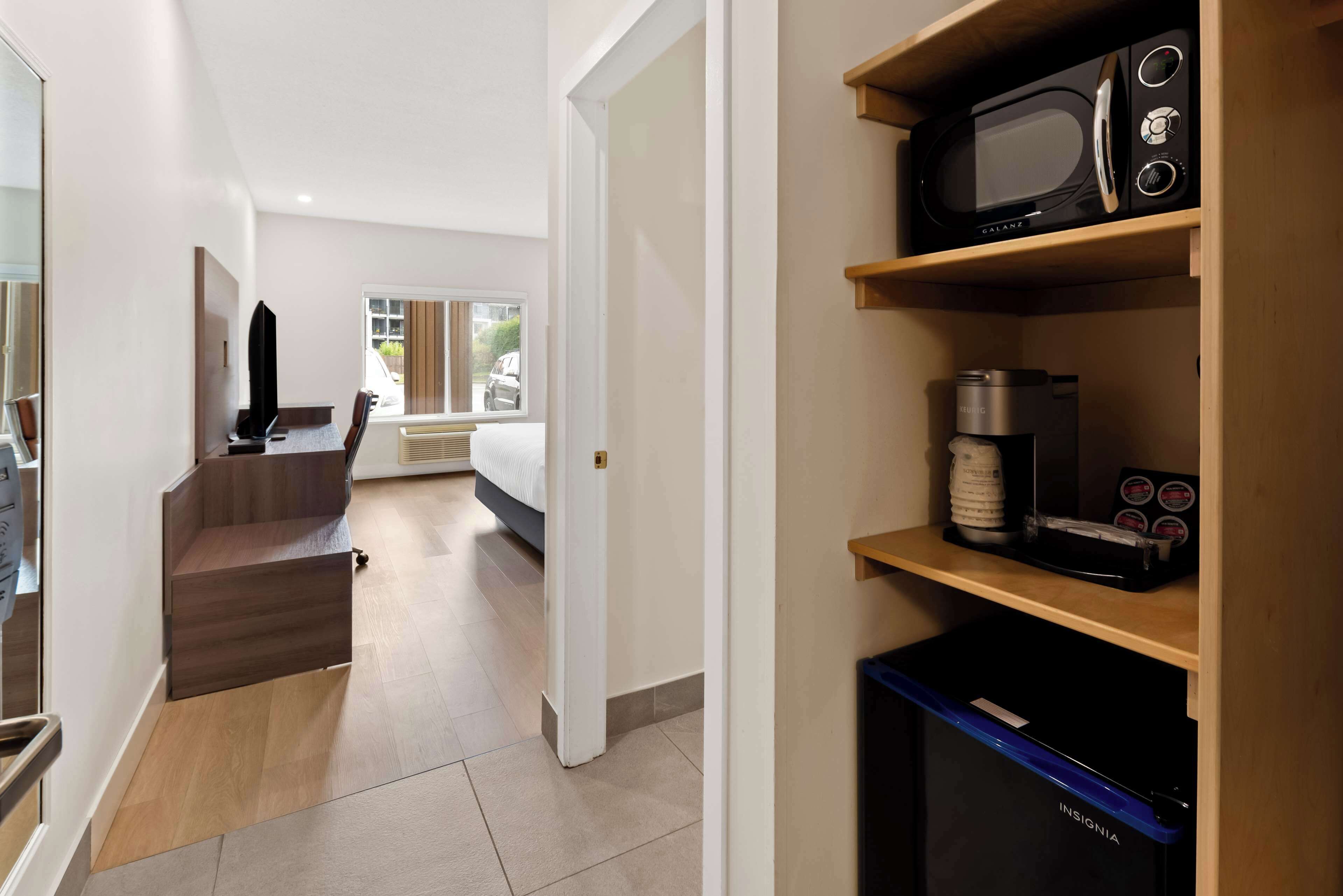 A hotel room with a bed, a desk, a microwave, a coffee maker, and a trash bin.
