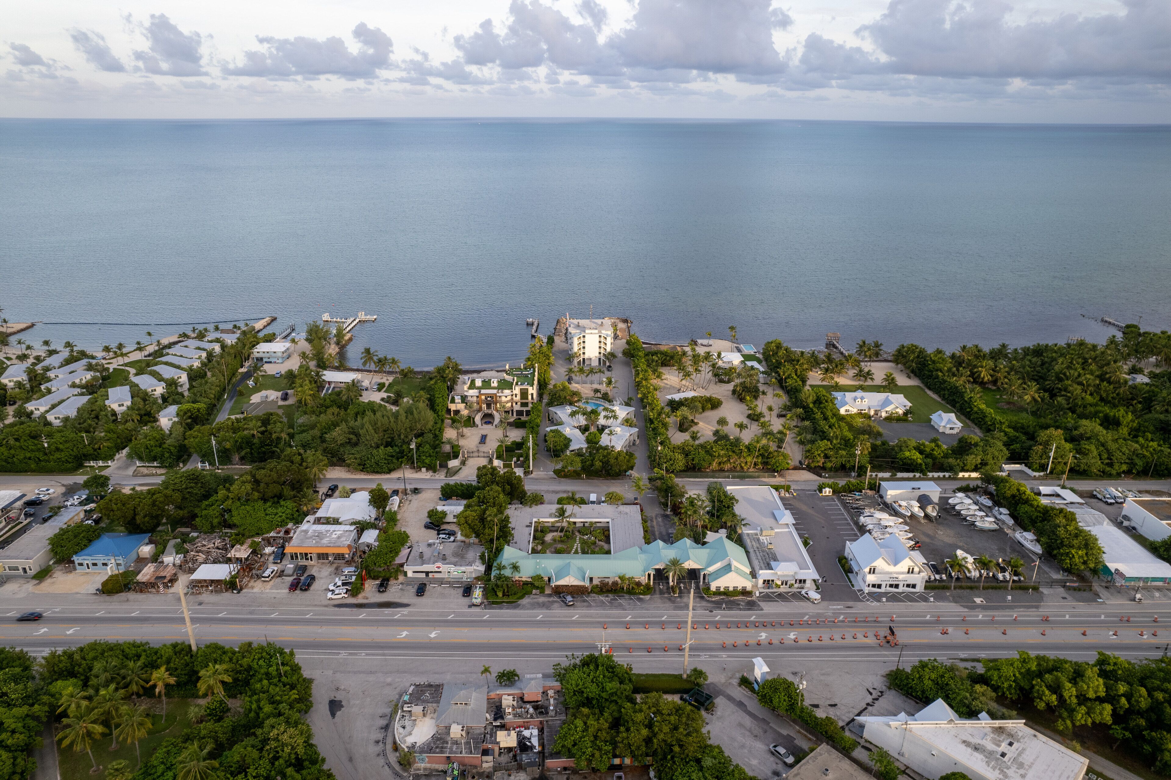 An aerial view of a coastal area with a marina, buildings, and roads.
