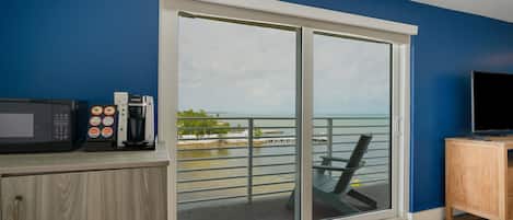 Una habitación con puerta corrediza de vidrio a un balcón, microondas, cafetera y televisor sobre un mueble de madera.