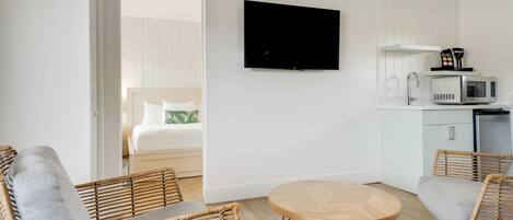 Une chambre d’hôtel comprenant un lit, deux fauteuils en osier, une petite table en bois, un téléviseur, un four à micro-ondes et une kitchenette.