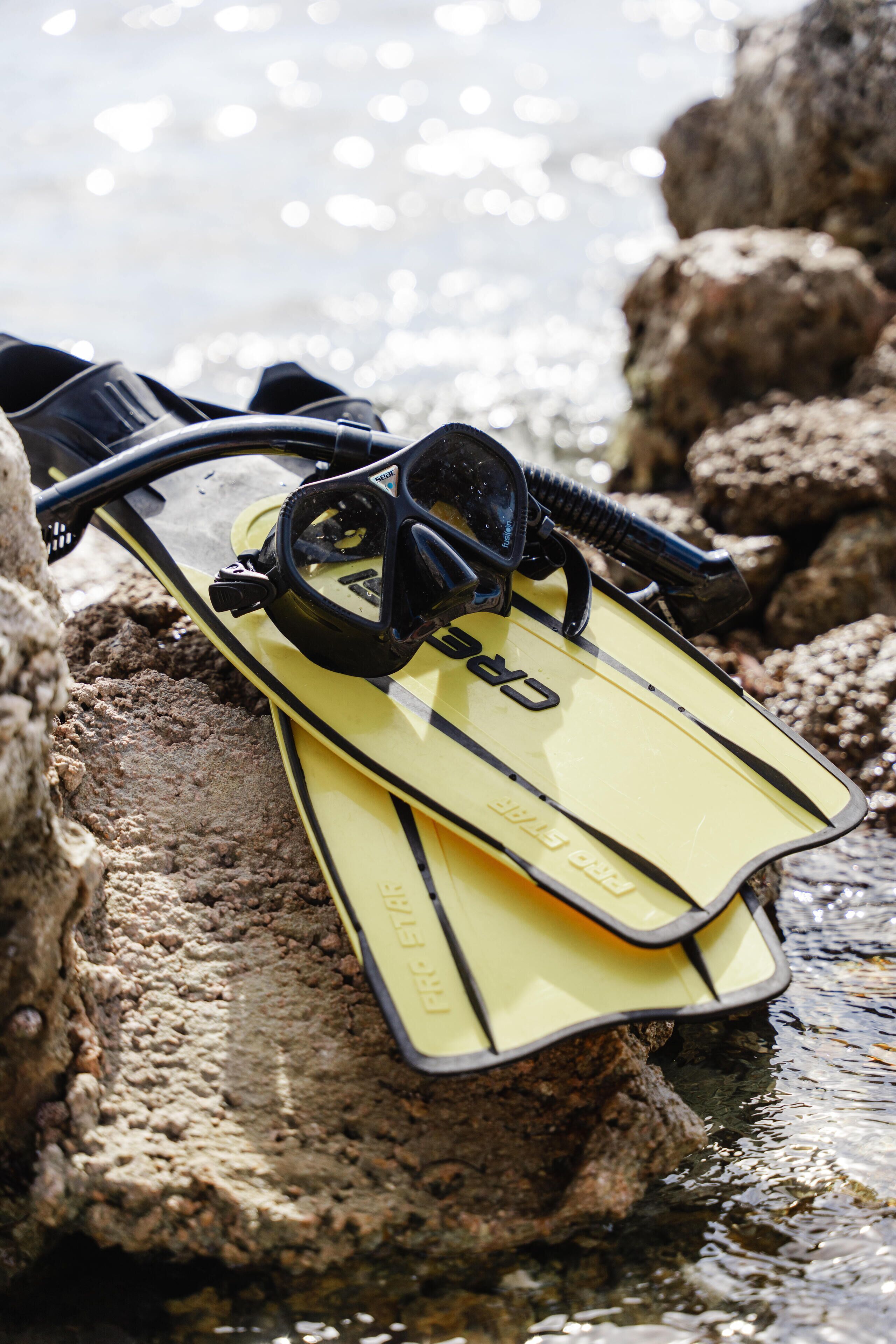 A pair of yellow flippers resting on rocks by a body of water.