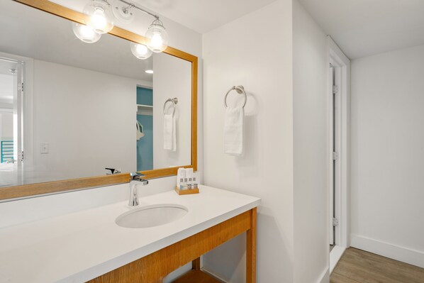A modern bathroom with a white sink, wooden vanity, and a large mirror with lights. - Hadley Resort and Marina (Islamorada)