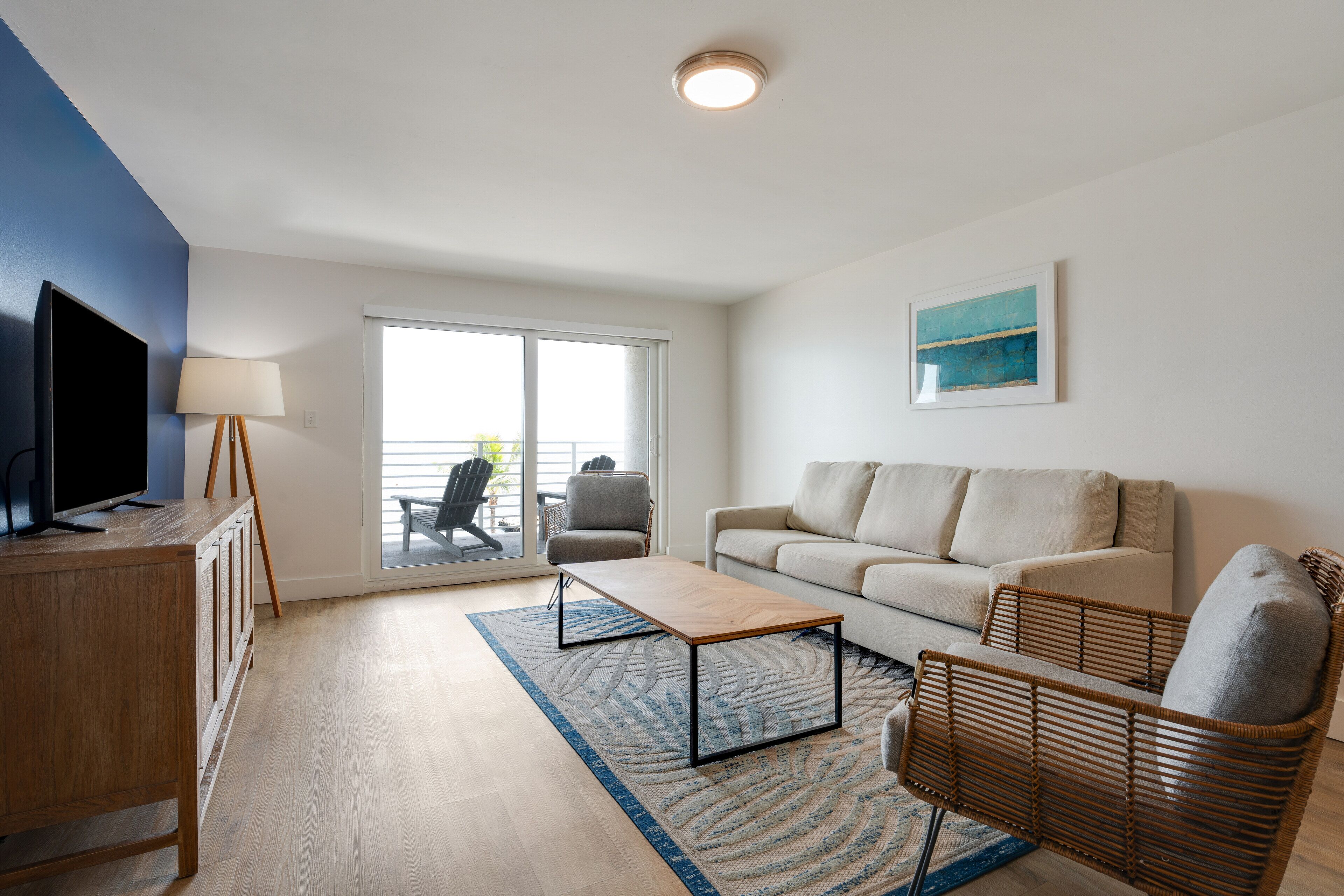 Ein modernes Wohnzimmer mit einer Couch, einem Couchtisch, einem Fernseher auf einer Holzkommode, einer Lampe und einem großen Fenster mit Blick.
