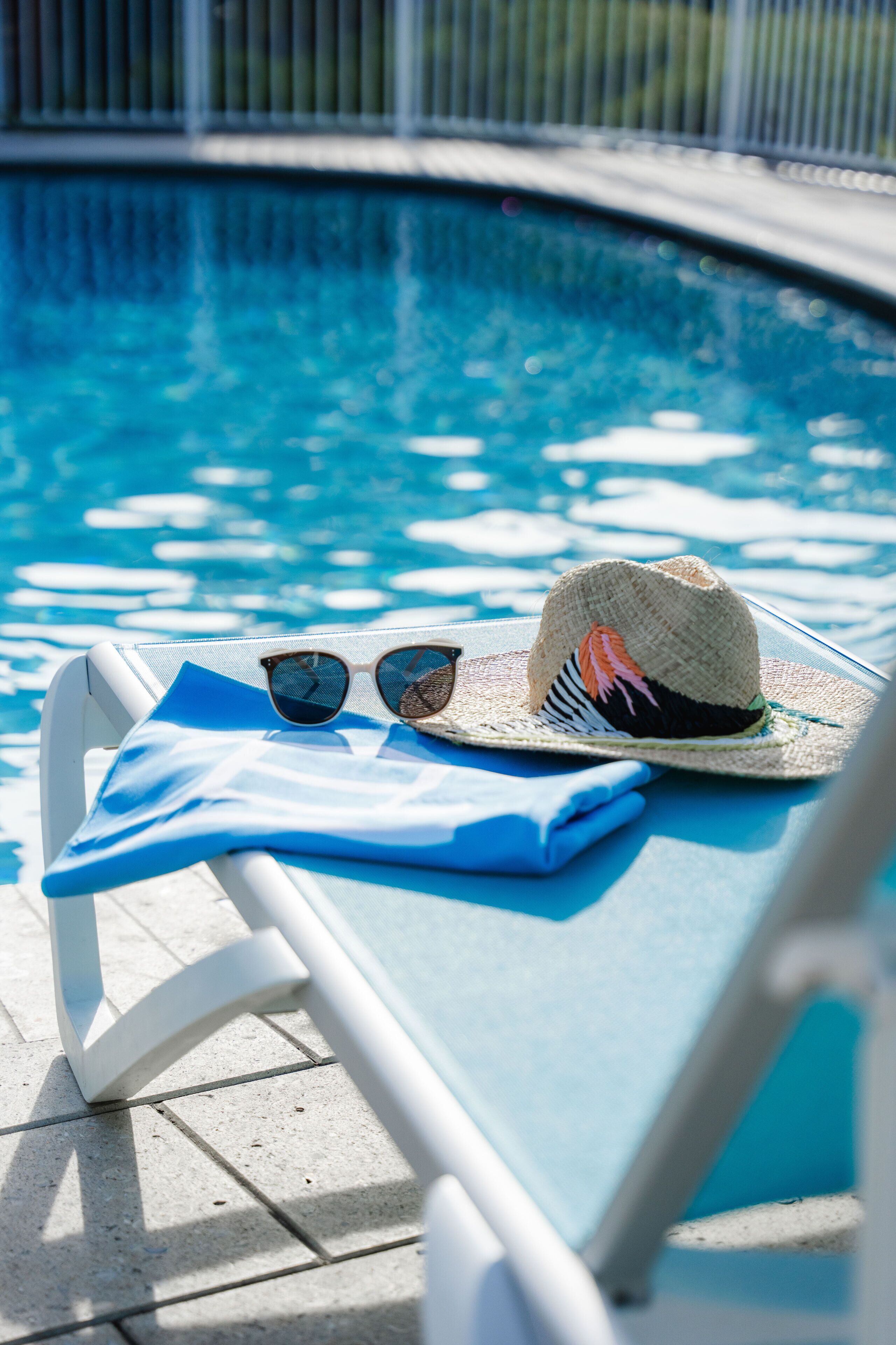 Escena junto a la piscina con una silla de descanso, un sombrero y gafas de sol sobre la silla.