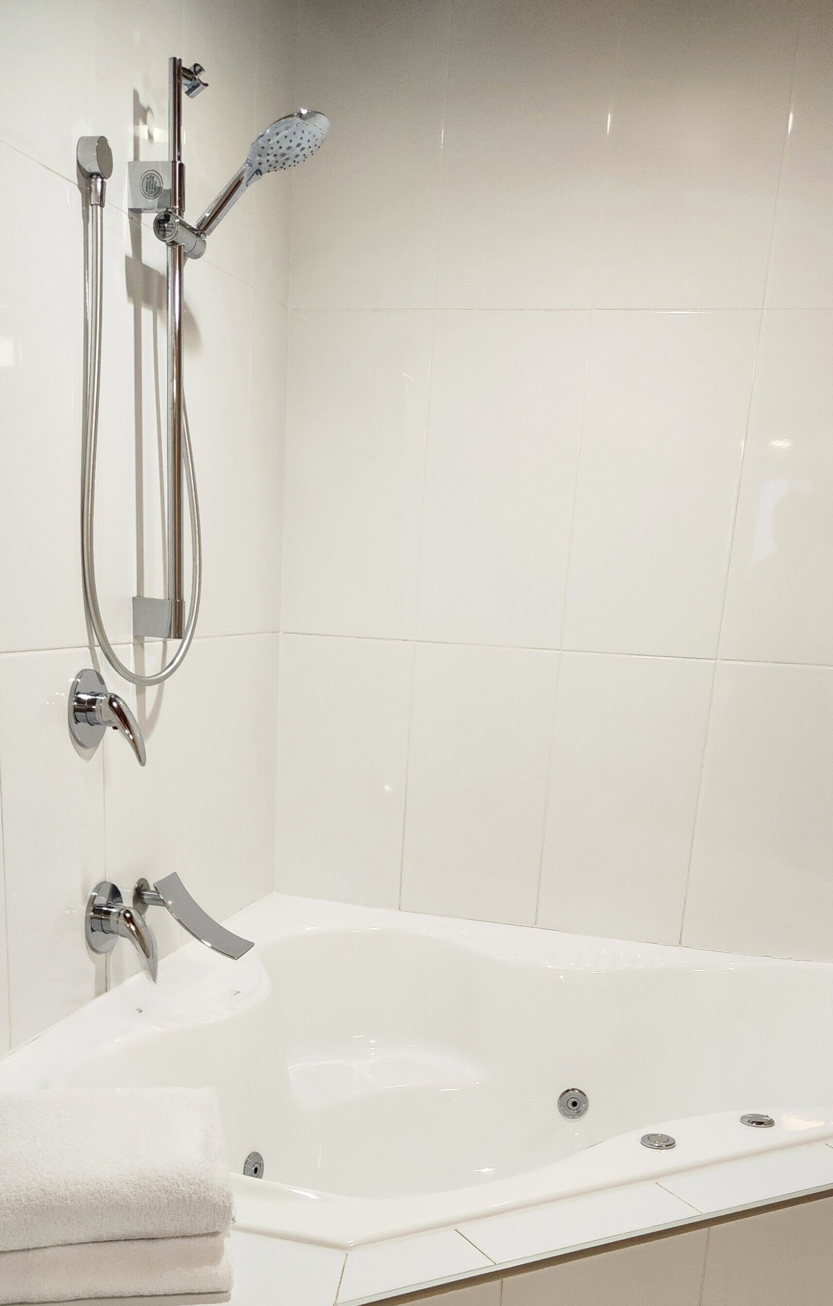 A bathroom with a white bathtub, a handheld showerhead, and a wall-mounted faucet.
