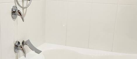 A bathroom with a white bathtub, a handheld showerhead, and a wall-mounted faucet.