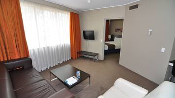 Et moderne hotelværelse med en lædersofa, et lille sofabord, et fladskærms-tv og en seng i baggrunden.