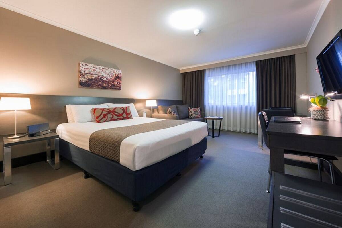 A hotel room with a large bed, a desk, a chair, a TV, and a painting on the wall.