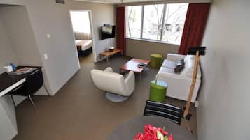 Una habitación de hotel moderna con cama, escritorio, televisor, sofá y mesa de comedor.