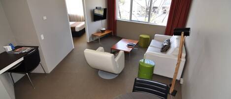 Una habitación de hotel moderna con cama, escritorio, televisor, sofá y mesa de comedor.