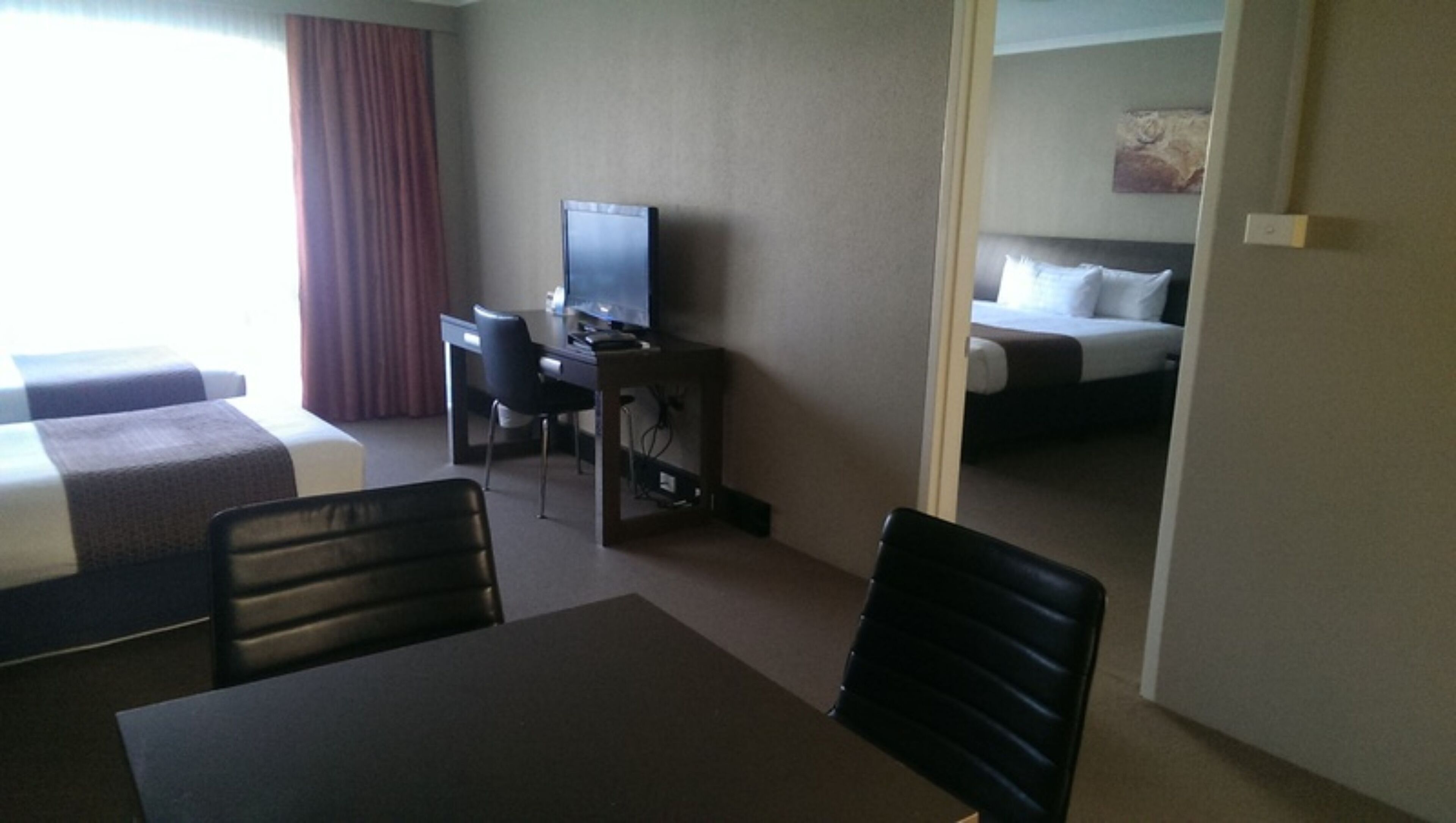 A hotel room with two beds, a desk with a television, and a dining table.