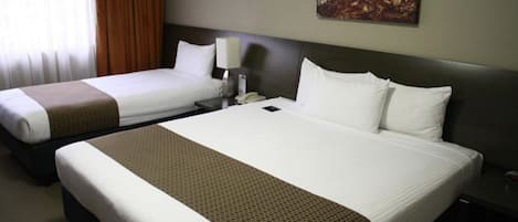 Una habitación de hotel con dos camas, una mesita de noche con lámpara y un cuadro en la pared.