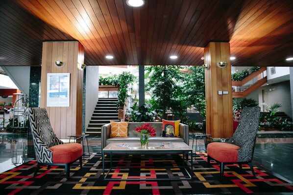 Un vestíbulo con techo de madera, un sofá, dos sillones, una mesa de centro y un tapete estampado.