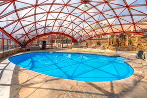 A large indoor swimming pool with a geodesic glass roof, stone flooring, and a stone wall with a water feature. - Baymont by Wyndham Durango (Durango)