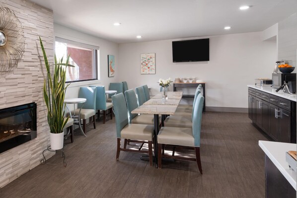 A modern dining area with a long table, chairs, a fireplace, and a kitchen area with cabinets and a TV. - Baymont by Wyndham Durango (Durango)