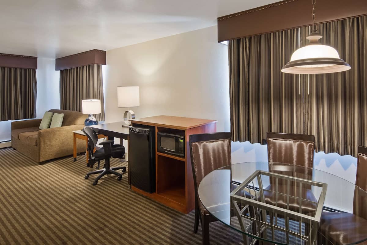A hotel room with a sofa, desk, chair, and dining table.
