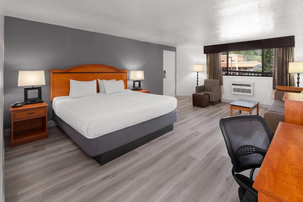 A hotel room with a large bed, two bedside tables with lamps, a chair, a desk, and a window with curtains.