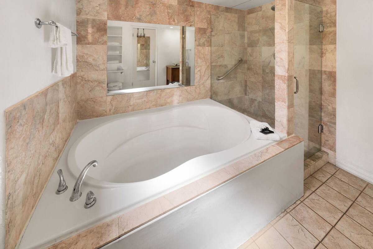 A modern bathroom with a freestanding bathtub, a glass-enclosed shower, and a marble-tiled wall.